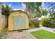 Quaint shed with a yellow exterior and blue doors, set amidst lush greenery and a brick pathway at 4105 W Bay Villa Ave, Tampa, FL 33611