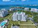 Aerial view of waterfront condo buildings showcasing lush greenery, swimming pool, and stunning city skyline views in the distance at 145 Belleview Blvd # 201, Belleair, FL 33756