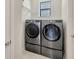 A laundry room has a modern washer and dryer with white shelving and neutral walls at 1476 Fort Cobb Ter, Wesley Chapel, FL 33543