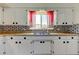 White kitchen with ample cabinet space, brick backsplash, and window with red curtains at 1516 Lemon St, Clearwater, FL 33756