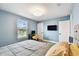 Bright bedroom with light wood-look floors, desk, TV, and a bed with grey comforter and yellow accents at 6700 Devlin Ln, Wesley Chapel, FL 33545