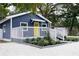 Exterior view of the home with blue siding, white trim, yellow front door, white rock ground cover, and landscaping at 8303 N 17Th St, Tampa, FL 33604