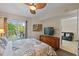 Bright bedroom with a ceiling fan, TV, and a sliding glass door to a balcony overlooking lush greenery at 11605 Gulf Blvd # 203, Treasure Island, FL 33706