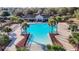 An aerial view of a vibrant blue community pool with palm trees, cabana, and ample lounging areas at 662 Petal Mist Ln, Brooksville, FL 34604