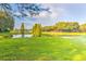 A serene view of a grassy field and pond reflecting trees and a building in the distance at 5212 Twin Creeks Dr, Valrico, FL 33596