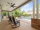 Covered outdoor patio featuring rocking chairs, a brick-paved deck, and a view of the fenced pool at 876 Ranch Rd, Tarpon Springs, FL 34688