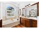 Bright bathroom with dual sinks, wood cabinets, and a soaking tub with a large arched window at 15045 Wind Whisper Dr, Odessa, FL 33556