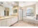 Bright bathroom featuring dual sinks, a soaking tub, glass-enclosed shower, and a large window at 4656 Copper Hill Dr, Spring Hill, FL 34609