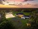 Picturesque aerial view of an equestrian estate featuring horse paddocks, barns, and a modern farmhouse at sunset at 11602 Innfields Dr, Odessa, FL 33556