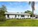 A single-story white home with a gray roof and well-manicured lawn in a lush setting at 1886 San Mateo Dr, Dunedin, FL 34698