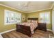 A bedroom with a wooden bed, white shutters, hardwood floors, olive green walls and a night stand with a lamp at 1748 Sunset Dr, Clearwater, FL 33755