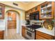 A kitchen area with stainless steel stove, tile floors, wooden cabinets, countertops, overhead microwave and an arched doorway at 1748 Sunset Dr, Clearwater, FL 33755