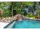 Backyard pool with a rock waterfall feature surrounded by lush tropical landscaping and trees at 1058 Roundstone Pl, Palm Harbor, FL 34683