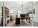 Bright home office featuring hardwood floors, a modern chandelier, and a large wooden desk with black accents at 11146 Rustic Timber Loop, San Antonio, FL 33576