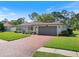 Single-story home with a brick driveway leading to the garage, framed by green lawns and landscaping at 2673 Clubhouse S Dr, Clearwater, FL 33761