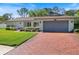 A single-story home with a brick driveway and two-car garage and mature landscaping at 2673 Clubhouse S Dr, Clearwater, FL 33761