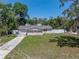 Aerial view of single story home with light siding, red shutters, a driveway and lawn surrounded by trees at 34477 Poinsettia Pl, Dade City, FL 33523
