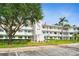 View of condo building with well-kept lawn, mature trees, turquoise accents, and flag at 8533 110Th St # 207, Seminole, FL 33772