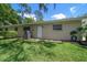 Back exterior of the home featuring a white door, greenery, and cooling system on a green lawn at 1431 Normandy Ln, Palm Harbor, FL 34683