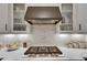 Close up of gas cooktop with white backsplash, counter seating, and modern vent hood at 14421 Swiss Bridge Dr, Lithia, FL 33547