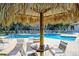 View of a poolside table and chairs under a tiki hut, with pool and lounge chairs in the background at 269 Madeira Cir, Tierra Verde, FL 33715