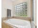 Modern bathtub with tile surround, complemented by a glass block window for natural light at 1727 Woodpond Way, Lutz, FL 33559