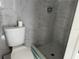 Bright bathroom featuring a tiled shower with gray tile floor, toilet, and marble-patterned tiled walls at 5151 Janice Ln, Holiday, FL 34690
