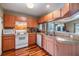 Kitchen featuring wood cabinets, white appliances, tile backsplash, and hardwood floors at 7508 S Mascotte St, Tampa, FL 33616