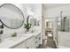 Modern bathroom featuring dual sinks, white cabinets, round mirrors, marble countertops, and a glass shower with marble tile at 10011 Parley Dr, Tampa, FL 33626