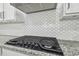 Close up of a kitchen cooktop with white tile backsplash and granite countertops at 6326 Waves End Pl, Apollo Beach, FL 33572
