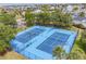 Aerial view of two blue tennis courts and community with mature trees and pond at 6533 Channelside Dr, New Port Richey, FL 34652