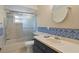 Cozy bathroom featuring tiled shower, vanity, and round mirror with decorative blue accent border at 6213 S Queensway Dr, Temple Terrace, FL 33617