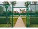 View of a green fenced community tennis court with palm trees and building visible from the entrance at 7040 Key Haven Rd # 601, Seminole, FL 33777