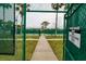 Entry to a community tennis court with posted rules, green fencing, palm trees and path through grass at 7040 Key Haven Rd # 601, Seminole, FL 33777