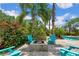 A backyard fire pit area with chairs, tropical flowers, and palm trees, adjacent to the refreshing pool at 9916 Preakness Stakes Way, Dade City, FL 33525