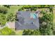 Aerial view of a home with a dark roof, screened-in pool, lush landscaping, and brick driveway at 19708 Wellington Manor Blvd, Lutz, FL 33549