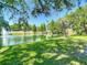 Beautiful view of a community pond with a fountain framed by trees and manicured grassy areas on a sunny day at 3611 Pine Knot Dr, Valrico, FL 33596