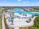 Aerial view of community lagoon featuring chairs, tiki huts, beach, and volleyball court near a residential neighborhood at 8919 Drummer Plank Dr, Wesley Chapel, FL 33545