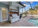 Outdoor kitchen with a stainless steel grill, brick backsplash, and access to the pool area in a screened enclosure at 2969 Talon Dr, Clearwater, FL 33761