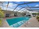 Beautiful in-ground pool featuring a screened enclosure, ladder, and lush landscaping with comfortable seating and outdoor cooking area at 2969 Talon Dr, Clearwater, FL 33761