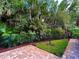 Lush backyard featuring a brick-paved patio, a well-maintained lawn, privacy fence, and lush tropical landscaping at 3240 Sand Key Dr, Palm Harbor, FL 34684