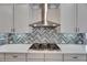 Close up of KitchenAid cooktop and stainless hood with herringbone backsplash and white quartz countertops at 5316 Candler View Dr, Lithia, FL 33547