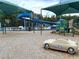 Community playground with blue slide, shade covers, and toy car on pea gravel base at 28451 Great Bend Pl, Wesley Chapel, FL 33543