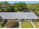 Low angle aerial of a flat-roofed home with light stucco and colorful shutters, a manicured yard, and lush, mature landscaping at 1535 Nursery Rd # 111, Clearwater, FL 33756