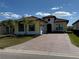 Inviting yellow home with a brick driveway, 2-car garage, and neat landscaping, under a sunny sky with scattered clouds at 2217 5Th E St, Palmetto, FL 34221