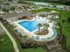 Aerial view of a community pool with lounge chairs, umbrellas and a splash pad surrounded by tropical landscaping at 17331 White Mangrove Dr, Wimauma, FL 33598