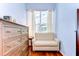 A comfortable sitting area includes a side chair and tall dresser, with hardwood floors and light filtering curtains at 5114 Whispering Leaf Trl, Valrico, FL 33596