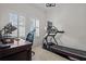 Home office with large windows, plantation shutters, desk, office chair, and treadmill at 14493 Promenade Pkwy, Odessa, FL 33556