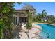 Covered patio features a ceiling fan, seating, and access to the in-ground pool with lush, tropical landscaping at 19 N Pine Cir, Belleair, FL 33756