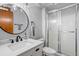 Well-lit bathroom featuring a frosted glass shower, a round mirror, a grey wall, and white cabinets and sink at 147 & 139 Edgewater Dr, Dunedin, FL 34698